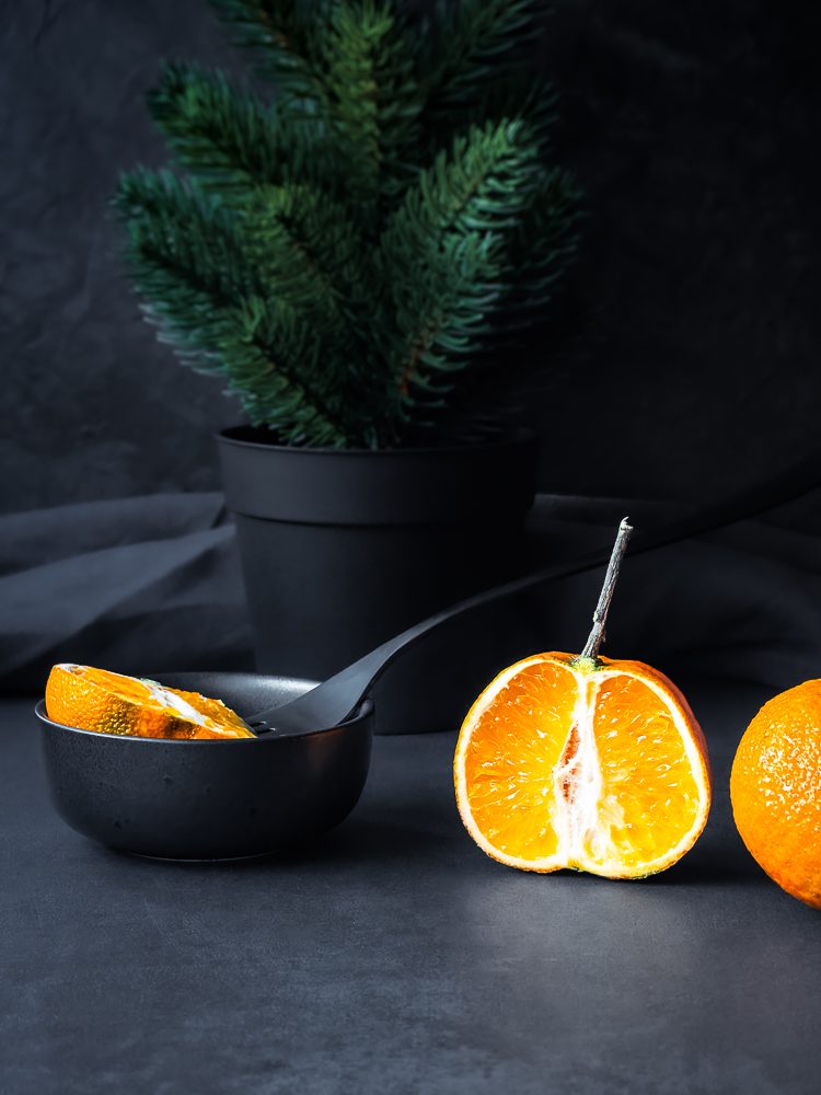 Durch die Mitte durchgeschnittene halbe Mandarine steht vor Tannengrün im Dank & Moody Style.